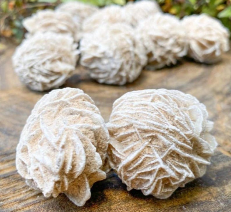 May include: Close-up of two white rose quartz crystals with a layered, rosette-like texture. The crystals are on a wooden surface.
