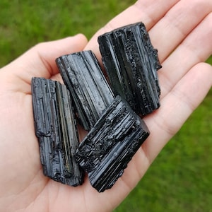 May include: Four black tourmaline crystals, also known as schorl, in various sizes and shapes. The crystals are raw and have a natural, rough texture.