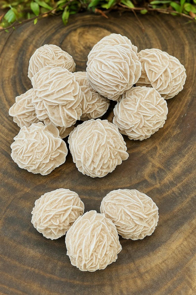 May include: A collection of 10 rose quartz crystals, also known as desert roses, on a wooden surface. The crystals are a light beige color and have a unique, layered, rosette-like formation.