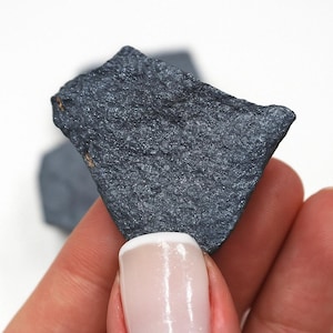 May include: A dark gray, rough-textured, irregularly shaped piece of hematite, a type of iron ore, held in a hand.