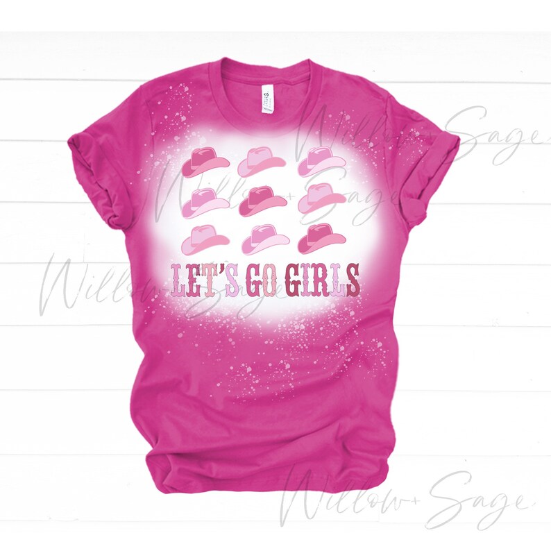 May include: Pink t-shirt with a bleach-splattered design featuring pink cowboy hats and the text "Let's Go Girls".