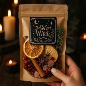 May include: A brown paper bag with a black label that reads "The Velvet Witch" contains dried orange slices, cranberries, cinnamon sticks, star anise, and pink crystals. The bag is held in a person's hand, with lit candles in the background.