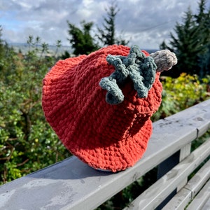 May include: A red crocheted bucket hat with a green crocheted leaf detail on top.