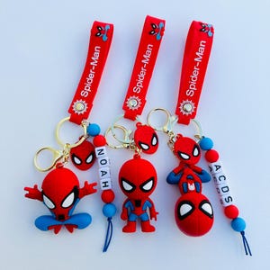 May include: Three red Spider-Man keychains with gold rings and charms. Each keychain has a different Spider-Man figure and a name spelled out with letter beads. The names are Noah, A, C, D, and S.