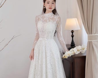 May include: A white lace wedding dress with long sleeves and a high neckline. The dress features a fitted bodice and a flowing skirt. The dress is adorned with delicate floral lace patterns. A white ribbon belt cinches the waist. The dress is suitable for a wedding or special occasion.