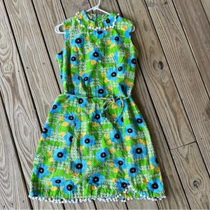 May include: A green and blue floral print dress with a white trim and a white pom-pom trim around the bottom hem.