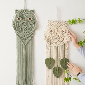 May include: Two macrame owl wall hangings, one in green and one in cream, with wooden bead eyes. Both hangings feature a fringe of tassels and leaves.