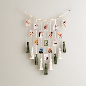 May include: A photo display with a string of wooden beads and green and white tassels. The photos are held in place with clothespins.