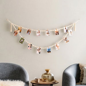 Peut inclure: Deux fauteuils gris avec des jet&eacute;s en fausse fourrure blanche et un coussin marron, face &agrave; face dans un salon. Une petite table noire avec un vase en verre dor&eacute; se trouve entre les fauteuils. Une guirlande de photos est accroch&eacute;e au mur au-dessus de la table.