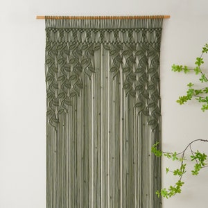 May include: A green macrame wall hanging with a leaf pattern. The hanging is made of thick cord and is attached to a wooden dowel.