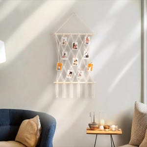 Pode incluir: Uma tape&ccedil;aria de macram&eacute; branca para pendurar na parede com uma barra de madeira e franjas de corda. A tape&ccedil;aria tem 12 espa&ccedil;os para fotos, cada um com um pequeno prendedor de madeira.