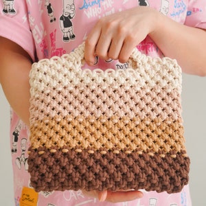 May include: A multi-colored crocheted tote bag with a white, pink, brown, and dark brown color scheme. The bag has a woven design and a handle.