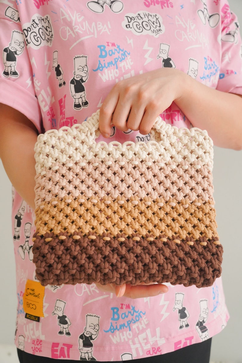 May include: A multi-colored crocheted tote bag with a white, pink, brown, and dark brown color scheme. The bag has a woven design and a handle.