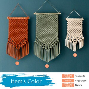 May include: Three macrame wall hangings in terracotta, sage green, and natural colors. The hangings are made with a knotted pattern and have fringe at the bottom.