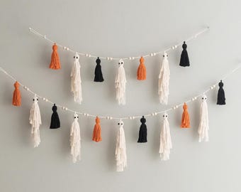 May include: A Halloween garland with white, black, and orange tassels strung on a white string with wooden beads.