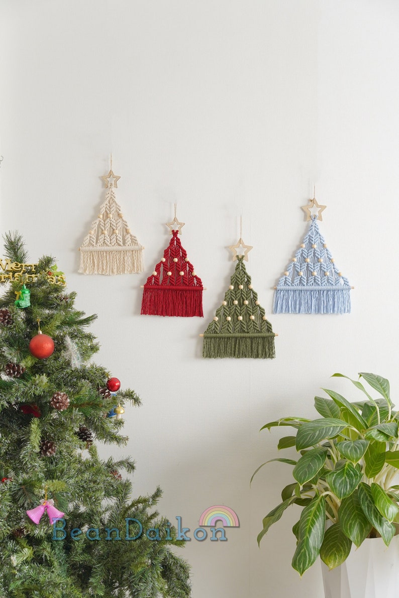 Puede incluir: Cuatro decoraciones de pared de &aacute;rbol de Navidad de macram&eacute; en diferentes colores: blanco, rojo, verde y azul. Cada &aacute;rbol tiene una estrella de madera en la parte superior y cuentas de madera tejidas en el dise&ntilde;o.