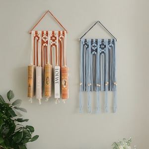 May include: Two macrame wall hangings with wooden dowels. The left hanging is orange and white with four books hanging from it. The right hanging is blue and white with wooden beads.