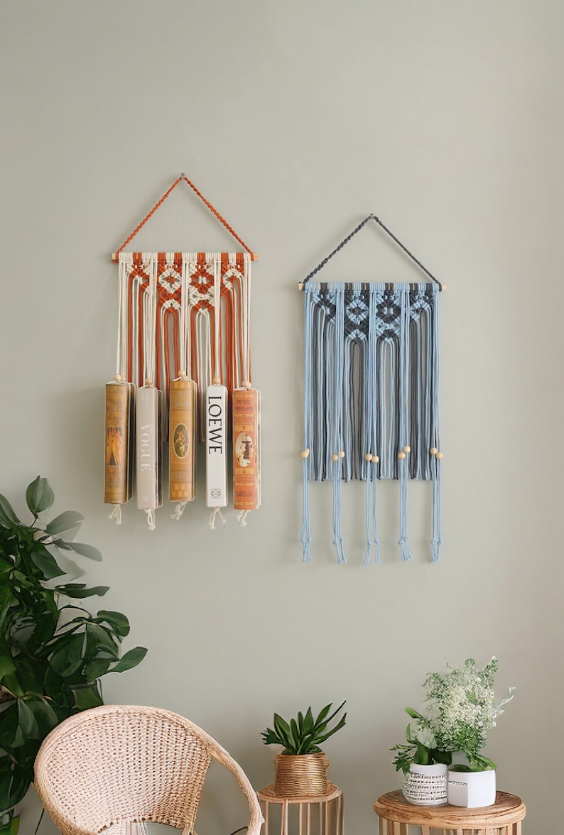 May include: Two macrame wall hangings with wooden dowels. The left hanging is orange and white with four books hanging from it. The right hanging is blue and white with wooden beads.