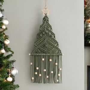 May include: A green macrame Christmas tree wall hanging with a wooden star at the top and wooden beads hanging from the bottom.