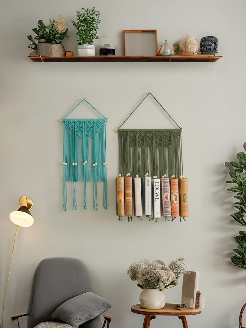 K&ouml;nnte beinhalten: Zwei Makramee-Wandbeh&auml;nge, einer in T&uuml;rkis und einer in Olivgr&uuml;n, mit Holzperlen. Der olivgr&uuml;ne Wandbehang hat eine Reihe B&uuml;cher davor.