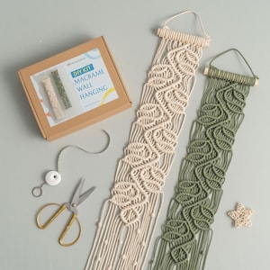 May include: DIY kit for making two macrame wall hangings. One is cream colored and the other is green. The kit includes yarn, a wooden dowel, and instructions.