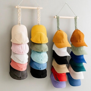 May include: A selection of baseball caps in diverse colours, such as yellow, pink, white, and blue, are displayed on wooden rods suspended by decorative macrame hangers. The caps are stacked vertically, showcasing a range of hues and styles.