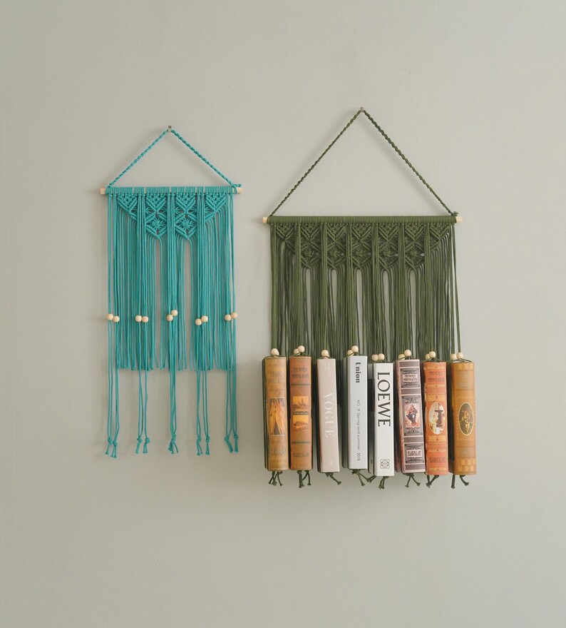 May include: Two macrame wall hangings with wooden beads. The top one is teal blue and the bottom one is green. The green one has books displayed on it.