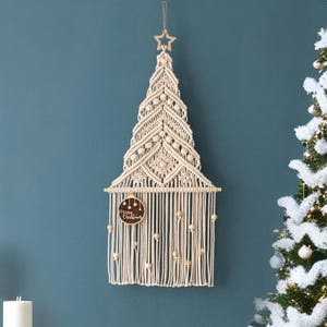 May include: A white macrame Christmas tree wall hanging with wooden beads and a wooden sign that says "Merry Christmas".