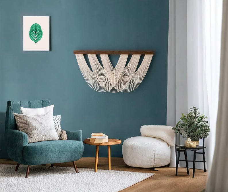 May include: A wall hanging featuring a dark wooden horizontal bar with off-white cotton cord draped in multiple overlapping U-shaped loops. The cord is attached to the top bar and hangs down in a symmetrical, layered pattern across the wall.