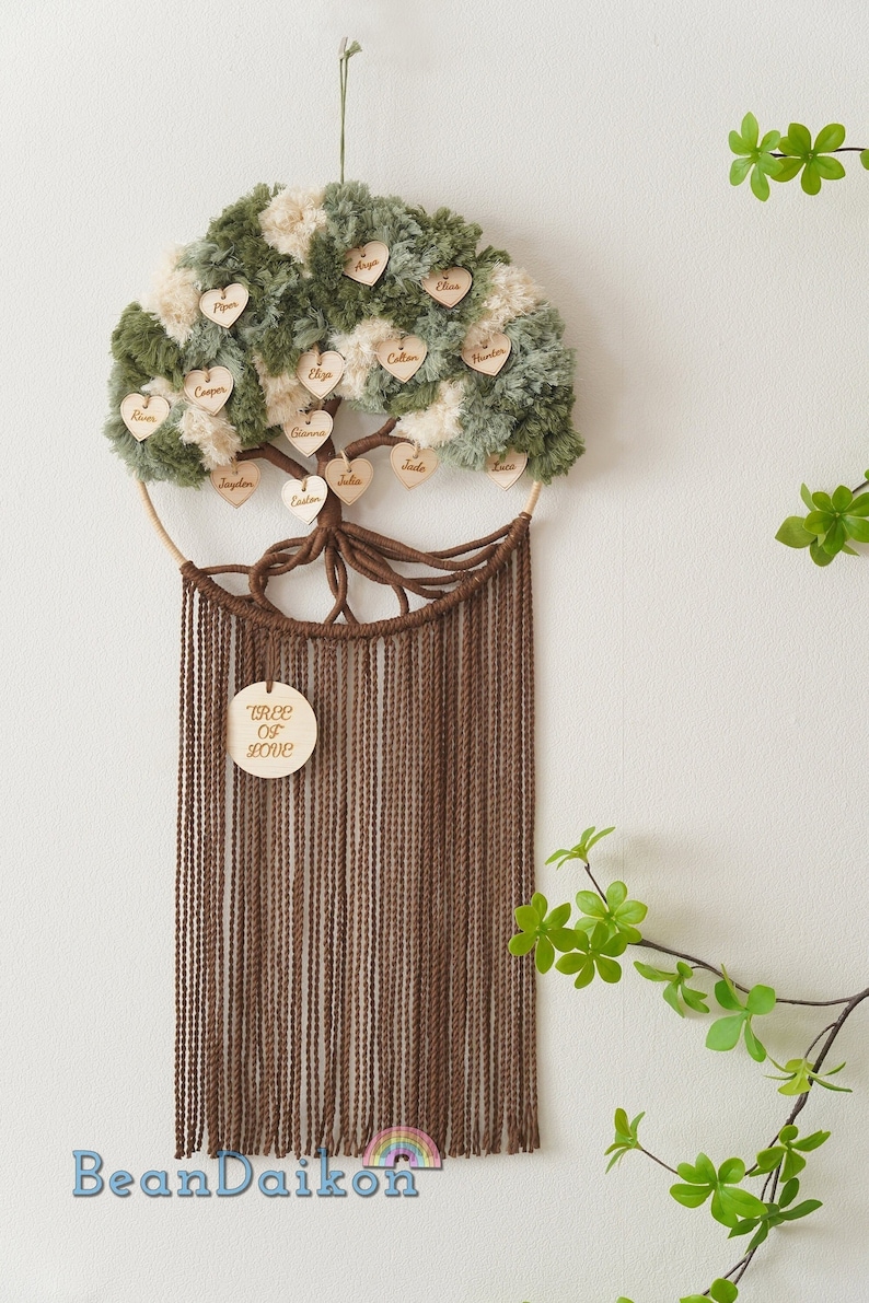 May include: A brown yarn dreamcatcher with a green and white pom-pom tree design. The tree has wooden hearts with names written on them. The dreamcatcher has a wooden circle at the bottom with the words "Tree of Love" written on it.