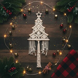 May include: A cream-coloured macrame wall hanging shaped like a Christmas tree, featuring intricate knotted patterns, wooden beads, and a star topper. The piece is suspended from a wooden dowel with long, fringed tassels hanging from the bottom.
