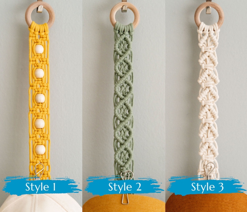 May include: Three macrame hat hangers in yellow, green, and cream colors. Each hanger has a wooden ring at the top and a metal clip at the bottom. Style 1 is yellow with wooden beads. Style 2 is green with a diamond pattern. Style 3 is cream.