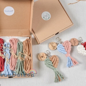 May include: A set of six colorful cotton cords in a cardboard box, along with four handmade heart-shaped keychains with personalized wooden tags. The keychains are made with a macrame technique and feature a variety of colors, including red, pink, blue, green, and white.