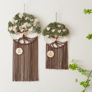 May include: Two green and white yarn pom-pom tree wall hangings with wooden hearts with names on them. The larger tree has the text "Tree of Love" on a wooden circle and the smaller tree has the text "The William Family" on a wooden circle.