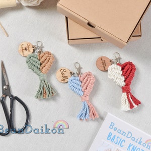 May include: Three handmade macrame heart keychains with wooden tags. The keychains are in different colors: green and beige, blue and pink, and red and white. The wooden tags have personalized text.