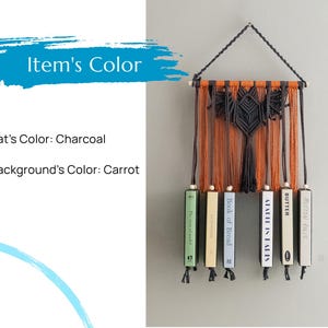 May include: A macrame wall hanging with a bat design in charcoal against an orange background. The hanging is attached to a set of books with titles including "A Table in Paris", "Butter", "Mutton Rolls", and "Book of Bread".
