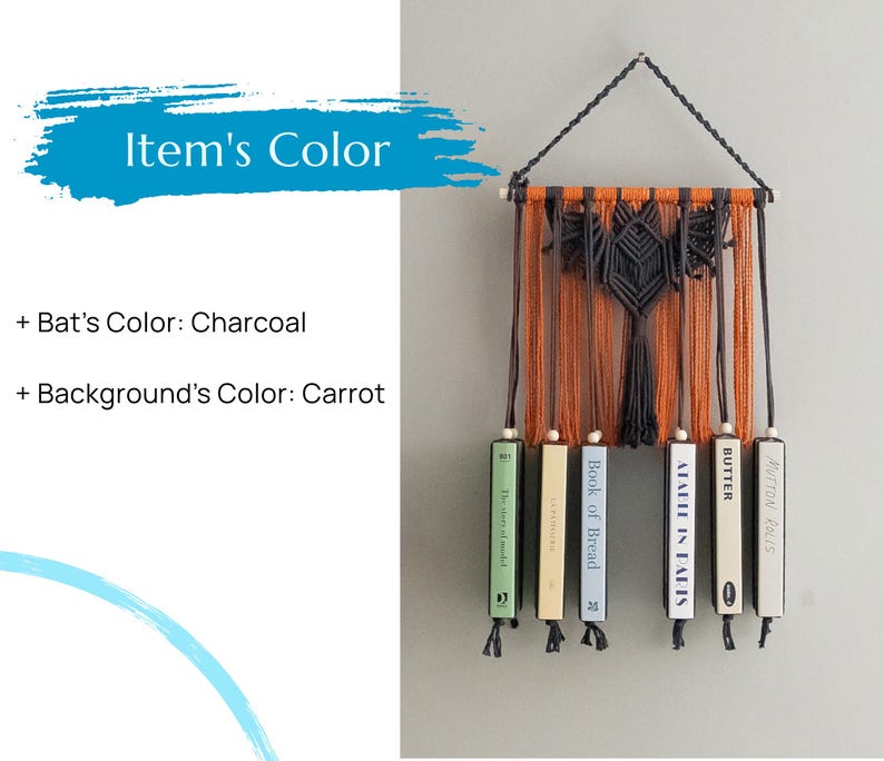May include: A macrame wall hanging with a bat design in charcoal against an orange background. The hanging is attached to a set of books with titles including "A Table in Paris", "Butter", "Mutton Rolls", and "Book of Bread".