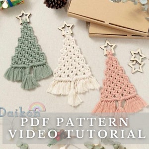 May include: Three macrame Christmas tree decorations in green, white, and pink with wooden star toppers. The decorations are hanging on a white background. PDF PATTERN VIDEO TUTORIAL is written in white text on a grey background.