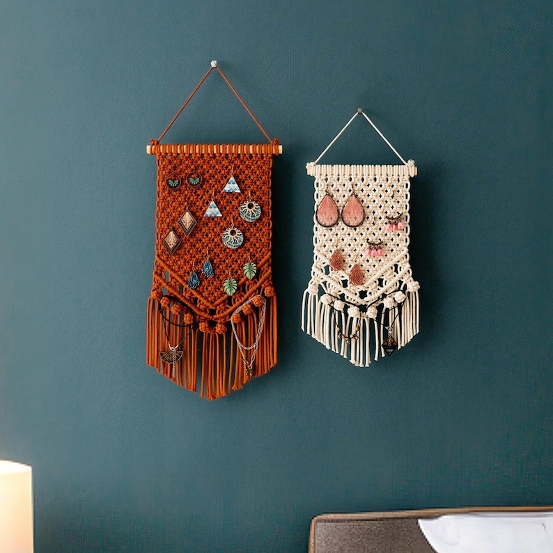 May include: Two macrame wall organizers with fringe, one in brown and one in white, with various earrings hanging from them.