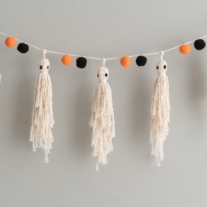 May include: A Halloween garland featuring white yarn ghost tassels and orange and black pom poms.