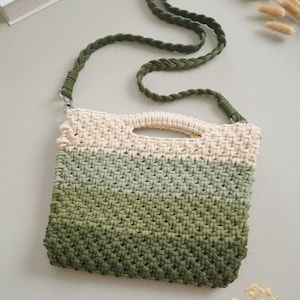 May include: A green, beige, and white crocheted bag with a long green braided strap. The bag has a woven texture and a rectangular shape.