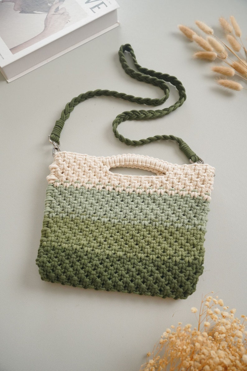 May include: A green, beige, and white crocheted bag with a long green braided strap. The bag has a woven texture and a rectangular shape.