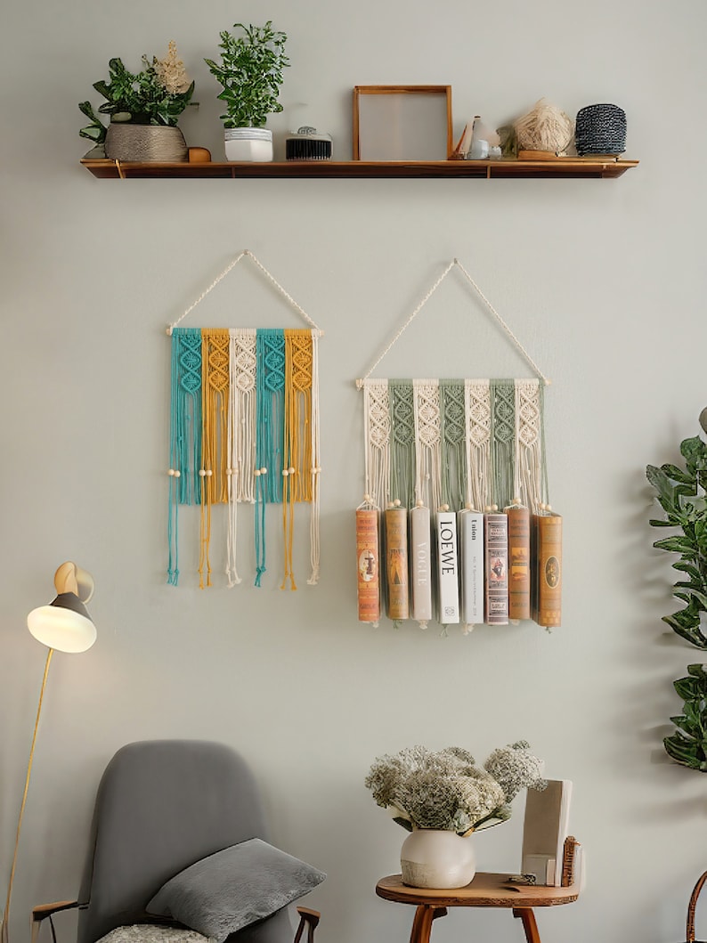 May include: Two macrame wall hangings, one with yellow, white and blue yarn and the other with green, white and beige yarn. The green, white and beige wall hanging has books displayed in the centre.