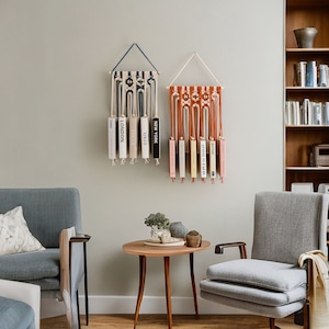 May include: Two macrame wall hangings with a blue and white pattern and a red and white pattern. Each wall hanging has a series of books hanging from it. The books have titles like "Vogue", "London", "New York", and "Butter".