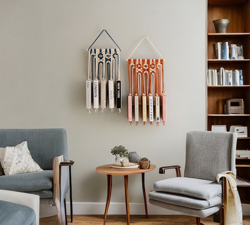 May include: Two macrame wall hangings with a blue and white pattern and a red and white pattern. Each wall hanging has a series of books hanging from it. The books have titles like "Vogue", "London", "New York", and "Butter".