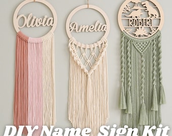 May include: Three DIY name sign kits with wooden hoops and macrame fringe. The hoops are decorated with the names "Olivia", "Amelia", and "Robert". The "Robert" hoop has a dinosaur design.