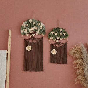 May include: Two brown macrame wall hangings with wooden circles that say "The Williams Family" and "Tree of Life". The circles are surrounded by green and white pom poms with names written on each pom pom.