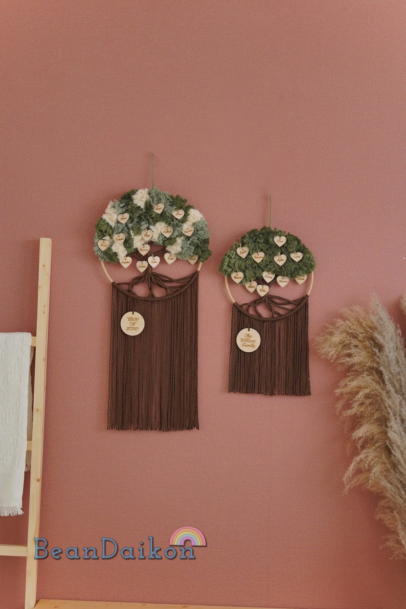 May include: Two brown macrame wall hangings with wooden circles that say "The Williams Family" and "Tree of Life". The circles are surrounded by green and white pom poms with names written on each pom pom.