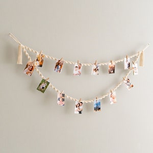 Peut inclure: Une guirlande de ficelle blanche avec des glands &agrave; chaque extr&eacute;mit&eacute;, tenant des photos de personnes avec des pinces &agrave; linge. Les photos sont dispos&eacute;es en ligne courbe.