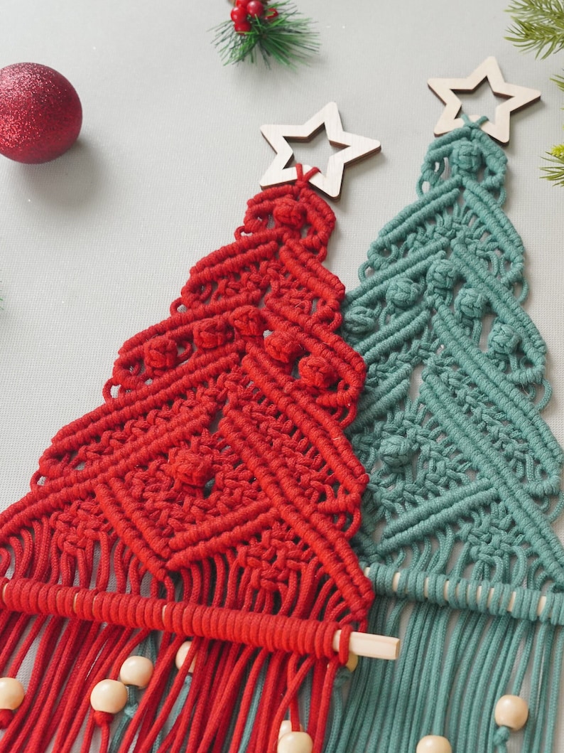May include: Two handmade macrame Christmas tree wall hangings. One is red and the other is teal green. Both have wooden stars at the top and wooden dowels at the bottom.